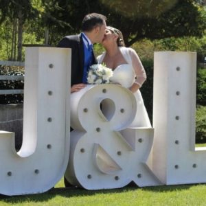 Recién casados besándose junto a letras gigantes 'J&L' de Animus Discotecas, una elección encantadora para decoración de bodas al aire libre.