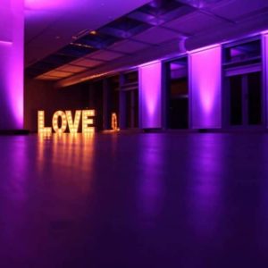 Letras gigantes 'LOVE' de Animus Discotecas iluminan con delicadeza un salón de eventos, bajo una atmósfera púrpura romántica para bodas.