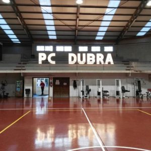 Letras gigantes 'PC DUBRA' de Animus Discotecas sobresalen en una pista de baloncesto, realzando la personalización del espacio para un evento deportivo.