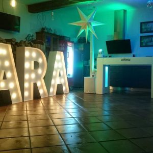 letras gigantes personalizadas iluminadas con el nombre 'YARA' y estación de DJ de Animus Discotecas Móviles, complementados con decoración estelar y ambiente acogedor para celebraciones personalizadas en Galicia.