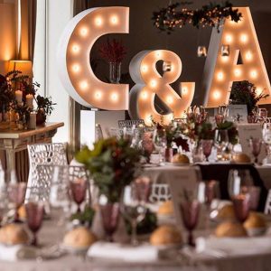 Letras gigantes 'C&A' iluminadas como pieza central en un salón de letras gigantes eventos, proporcionando un ambiente cálido y personalizado para una boda elegante.
